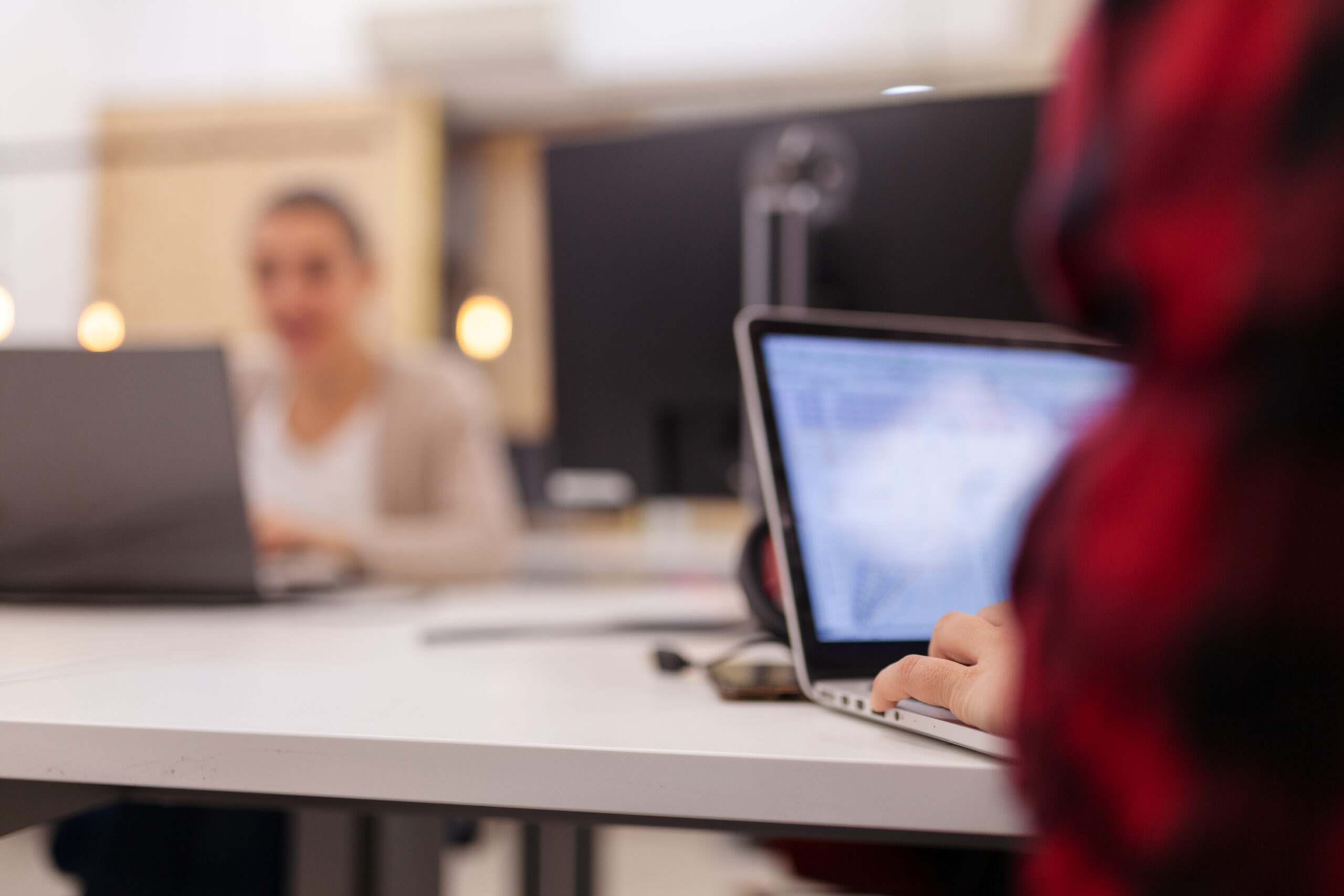 Girl working on laptop computer in an office. Abstract screen with focus on hands. People working in the background.