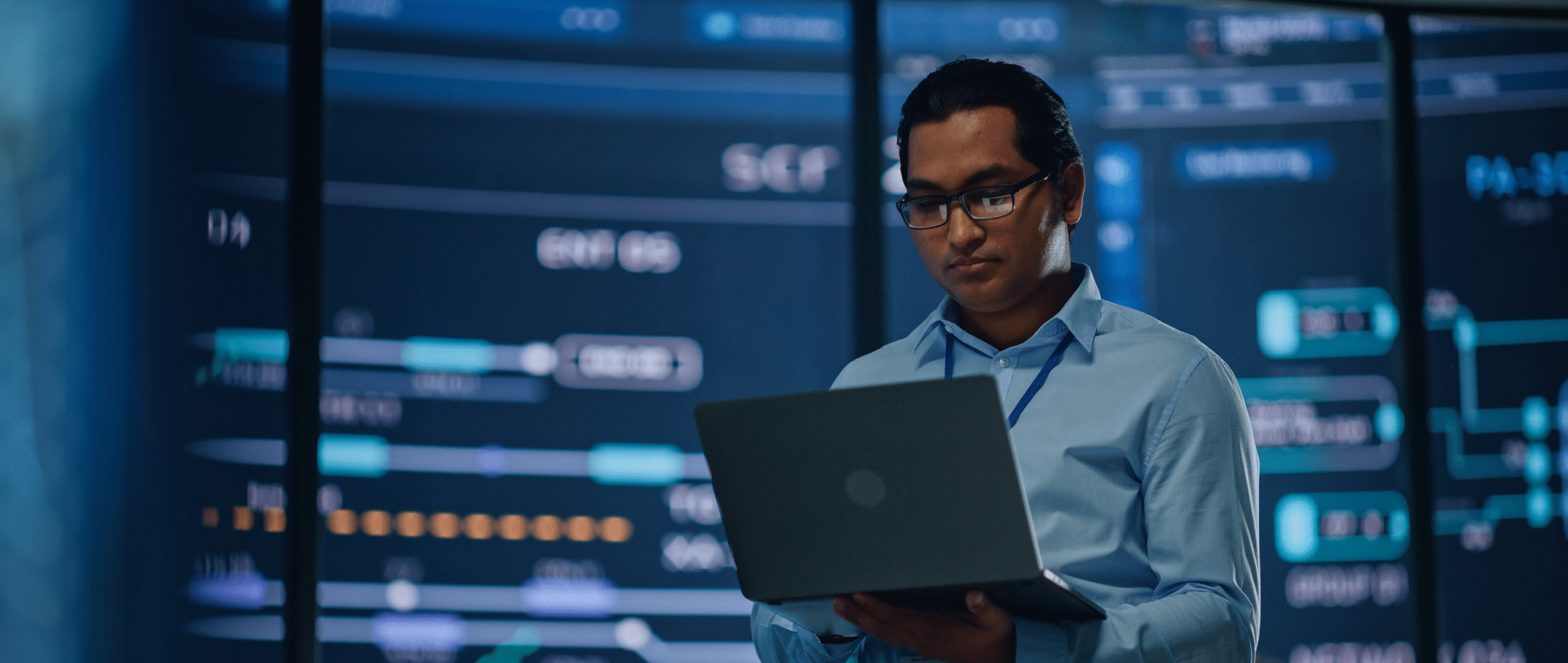 Cyber professional working on a laptop in front of control centre