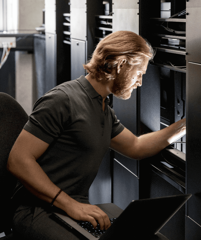 Cyber expert working in a server room on a laptop